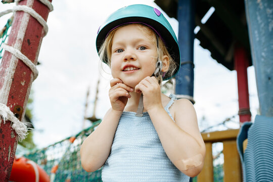 Smiling girl fastening sports helmet at rope park