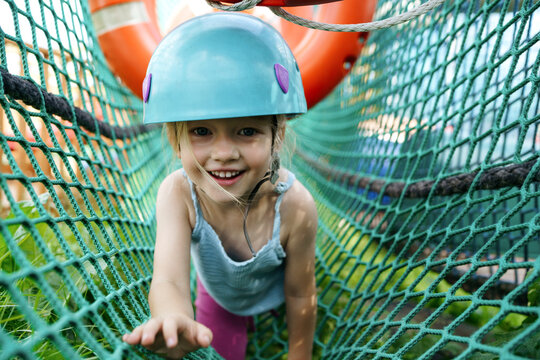 Smiling girl crawling on net at adventure park