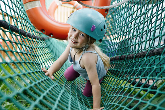 Happy girl wearing helmet and crawling on net at park