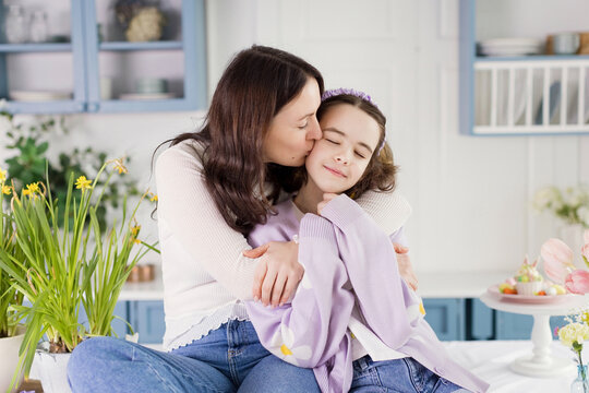 Mother kissing daughter sitting on table amidst Easter decorations at home