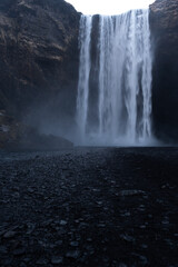 The powerful presence of Skogafoss waterfall in Iceland cascades over a towering cliff into a rocky...
