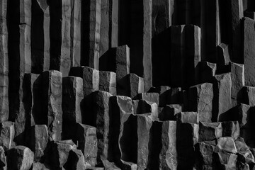 Dramatic black and white background capturing the stark geometry of towering basalt column formations at Black Sand Beach, Vik in Iceland - obrazy, fototapety, plakaty
