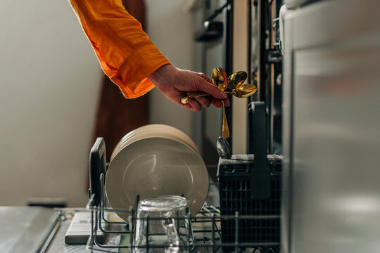 Woman picking up washed spoons from dishwasher at home