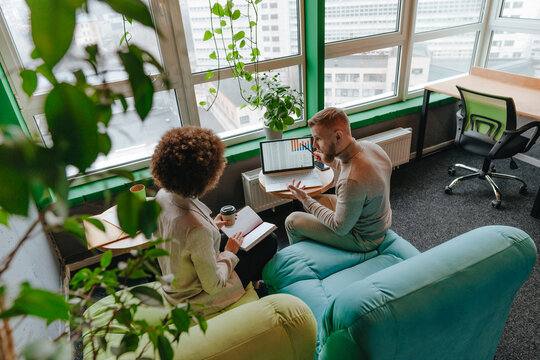 Multiracial business colleagues discussing graph on laptop in meeting at coworking office