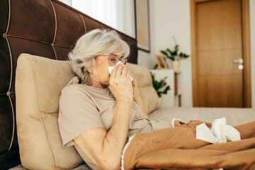 An ill senior woman with flu is lying in bed in a bedroom.