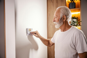 A senior man is adjusting central heating on dashboard at home.