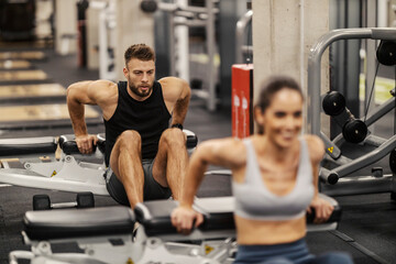 Strong sportsman is doing dips on a bench with a sportswoman in a gym.