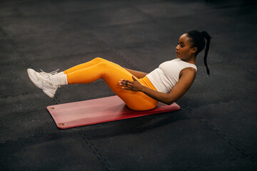 A fit african american sportswoman is doing abs at the gym.