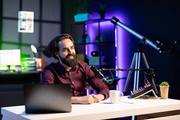 Happy internet star using quality mic in studio to discussing with viewers. Smiling man sitting at...