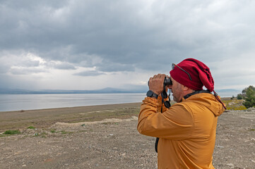 A man birdwatching with binoculars on a lake.