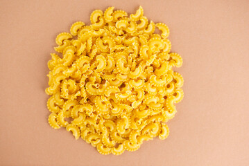 Heap of Creste Di Gallo raw pasta on a brown background. Rooster scallop. Top view.