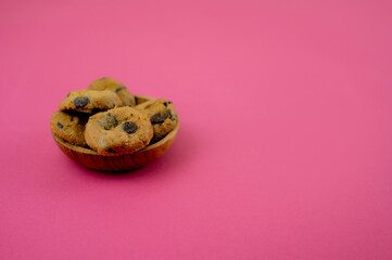 Chocolate chips cookies served on a small wooden bowl, isolated on pink background. A close-up and selective focus photo of the cookie. A copy space.