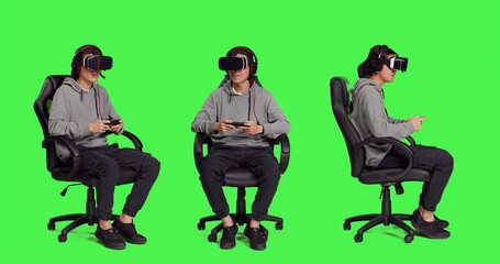 Person rests on chair over greenscreen backdrop and performs video games using virtual reality eyewear and mobile device, takes part in online multiplayer contest. Asian guy loving combat games.