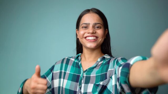 Young woman taking selfie portrait, POV shot of a beautiful Asian Indian girl taking her picture and showing thumbs up gesture