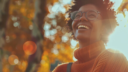 Joyful woman in an autumn setting with sunlight filtering through leaves. - obrazy, fototapety, plakaty