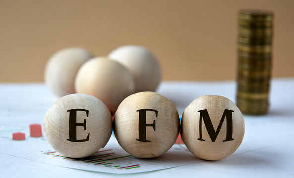 EFM - abbreviation on wooden balls on a background of coins and graphics.