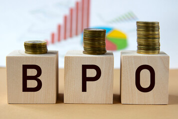 BPO - abbreviation on wooden balls on a background of coins and graphics.