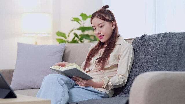 Asian businesswoman working from home, reading her work notebook on the sofa in the living room