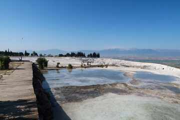 View from the travertine terraces of Pamukkale onto the valley with a paraglider in the background,...
