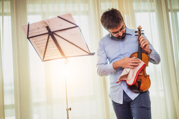 Man playing violin at home. He is cleaning his instrument.