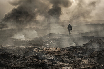A lone figure walks through a desolate, smoky landscape evoking a post-apocalyptic scene.