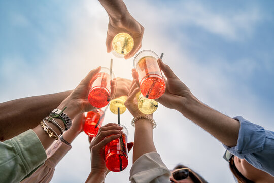 Group of friends toasting with colorful drinks - summer celebration, joyful moments, outdoor party vibe - happy young adults raising drinks in the sky.