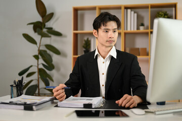 Naklejka premium Handsome businessman in black suit watching online webinar on computer display at office