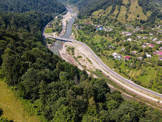 Fototapeta na wymiar view of a road in the mountains, a river flows between the bridges, a village is located along the road between the mountains, a summer landscape