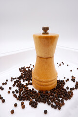 Pepper grinder with black peppers placed on a white tray. Wooden bottle for pepper with rustic style kitchen. Black pepper is healthy ingredient for cooking. Herb and spice idea with white background.