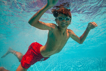 Smiling teen boy in water goggles is captured underwater swim