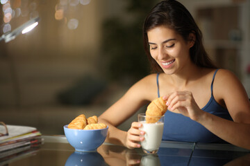 Happy woman in the night dipping bakery in milk