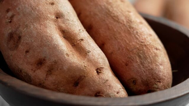 Uncooked sweet potato (yam) in kitchen wooden bowl. Unpeeled whole batata roots. Vegetable diet ingredient. Rotation