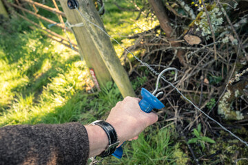 Farmer seen attaching a metal hook to a livestock electric fence. Once hooked, the electric fence is live. Used to keep livestock from escaping the paddock.