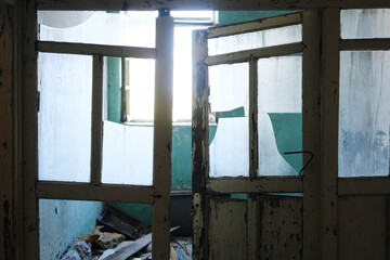 Ruined Interior of Abandoned Building Through Broken Window. A view through a broken window reveals the decaying interior of an abandoned building with peeling paint and debris.