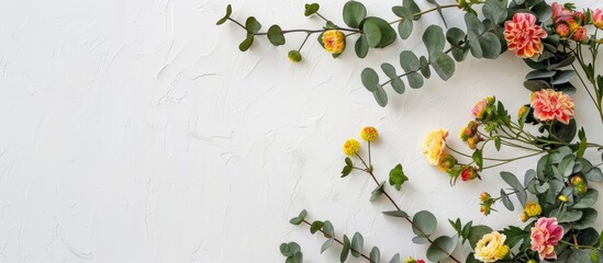 A floral arrangement featuring a circular design of yellow and pink flowers, intertwined with eucalyptus branches, set against a white backdrop.
