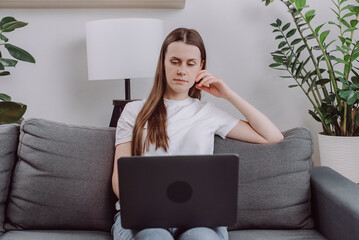 Focused cute young caucasian woman sitting alone on cozy sofa working on laptop. Freelancer in calm and cozy living room coding. Remote working in comfortable environment. Business concept