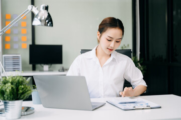 Obraz na płótnie Canvas Asian Businesswoman Analyzing Finance on Tablet and Laptop at Office Desk tax, report, accounting, statistics, and analytical research concept
