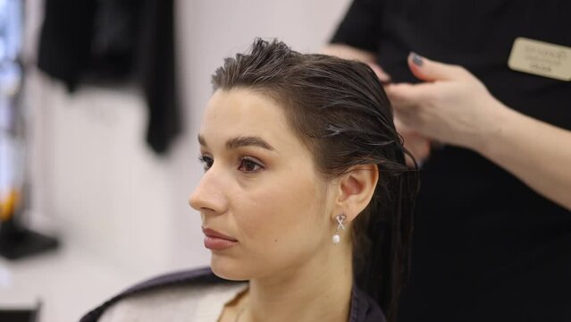 happy woman with short brunette hair sitting in hairdressing cape in beauty salon, getting haircut by professional hairdresser.girl doing keratin treatment.curls at the end.wet hair,towel on head.4k
