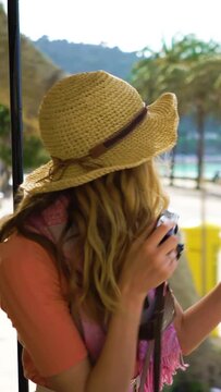 A young woman wearing straw hat enjoying traveling on an old tram or train along sea coast, taking pictures of beautiful tourist locations using vintage camera. A vertical video.