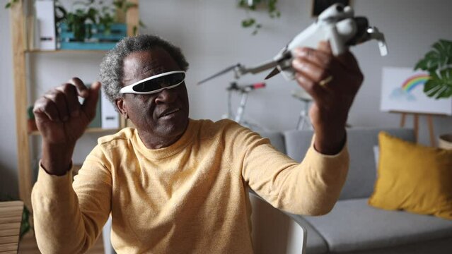 Elderly Man with 3D Glasses Enthusiastically Flying a Drone Indoors - Amused senior man in 3D glasses piloting a drone inside, technology enjoyment at home.