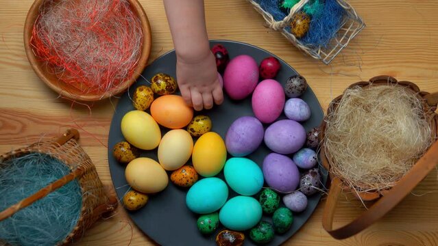 Easter table setting for the festive meal: Top view of the children's hands taking colored quail Easter eggs from the grey plate