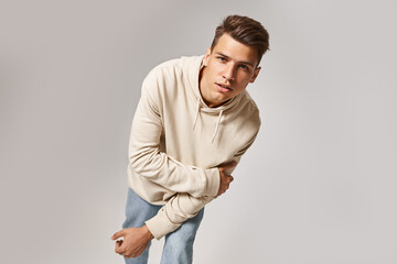 handsome young man leaning to forward and holding to arm against grey background