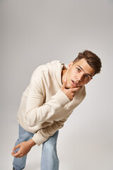 charismatic young guy leaning to forward and touching to jawline against grey background