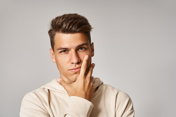 portrait of handsome young man with brown hair and grey eyes covering to cheek with hand