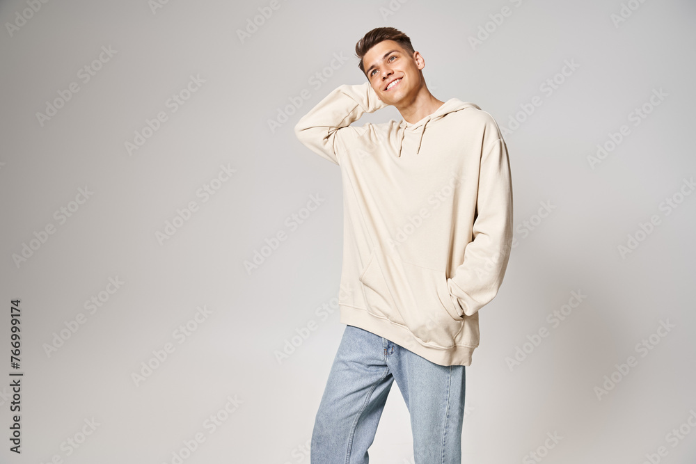 Wall mural attractive man in white hoodie putting hand behind head and looking to up against light background