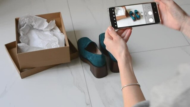 A young woman takes pictures of shoes with a smartphone to sell online. Second hands, second life of things. Online store for selling used items.