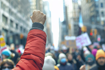 Close up of a fist raised in the air at an outdoor political protest - obrazy, fototapety, plakaty