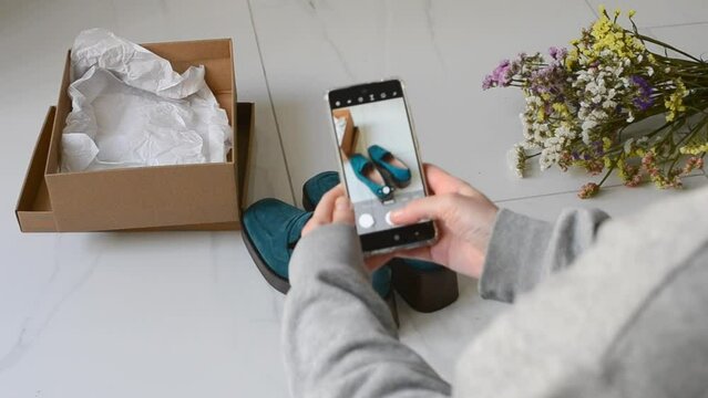 Young woman with a smartphone takes pictures of shoes to sell online. Second hands, second life of things. Online store for selling used items.