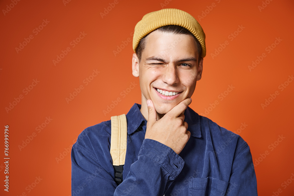 Wall mural portrait of charming young man in yellow hat with grey eyes winking and touching to chin with hand