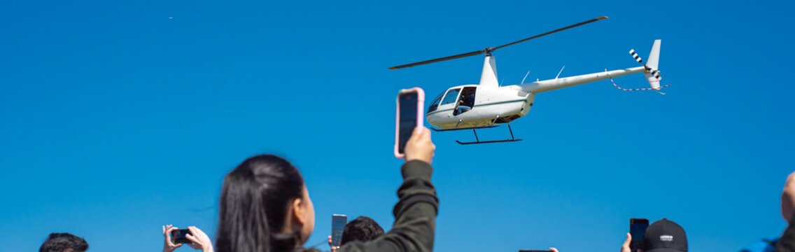 Panorama view hands taking photo hovering helicopter drops colorful eggs and goodies at Easter event in Richardson, Texas, rear view diverse group of people with mobile phone, Chistian tradition